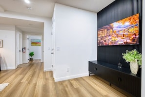 A modern interior with a wooden floor, a black entertainment unit, and a large TV displaying a scenic landscape. - Welcome to Sapphire Inn which is 13  minutes from YYC Calgary Airport (Calgary)