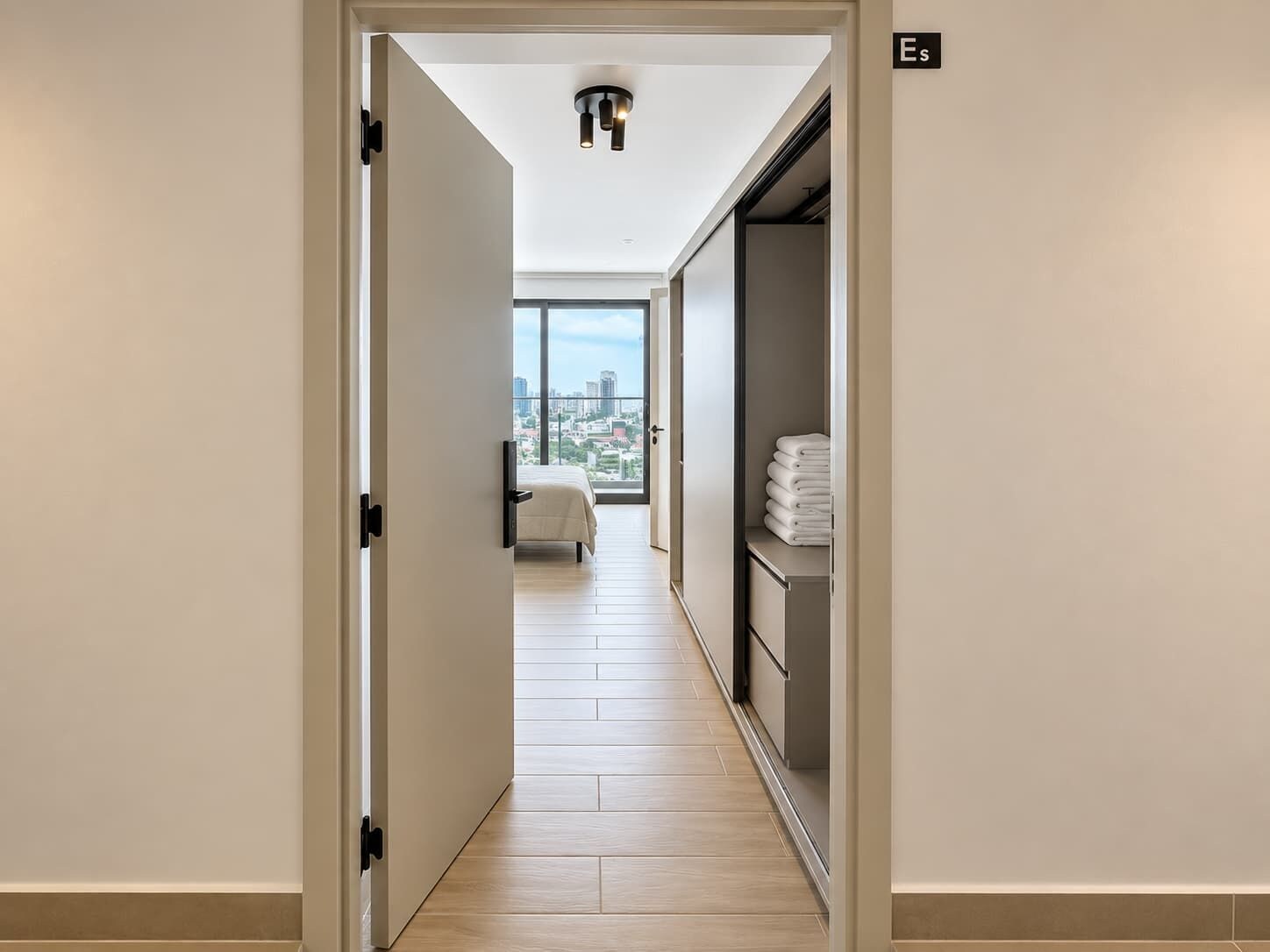A hotel corridor with a bed, a wardrobe, and a view of the city.