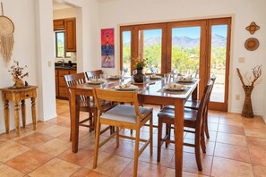 A dining area with a large table set for six, wooden chairs, and a view of the outdoors through a sliding glass door. - Cave Creek Desert Dream — 3BR Main House (Cave Creek)