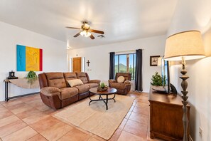 A living room with a brown leather sofa, a recliner, a coffee table, a lamp, and a ceiling fan. - Cave Creek Desert Dream — 3BR Main House (Cave Creek)