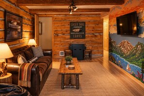 Een gezellige kamer met een houten logwand, een wandtelevisie, een lijst met afbeelding, een bank, een bijzettafeltje en een schilderij van een landschap.