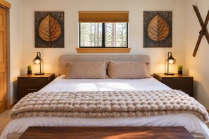A bedroom with a large bed, two bedside tables with lamps, a window with blinds, and two wall-mounted leaf artworks. - Lakeview Retreat Walk to Town + Fenced Yard (Grand Lake)