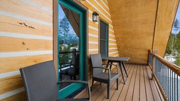 Een houten terras met twee rieten stoelen en een kleine tafel, een glazen deur naar buiten en een lantaarn aan de muur.