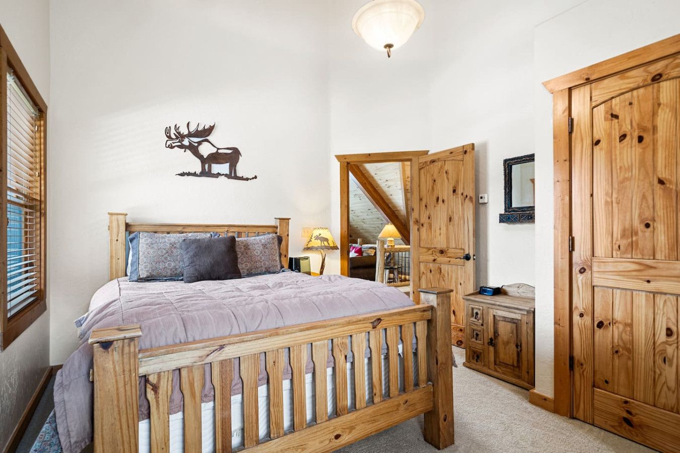 Een slaapkamer met een houten bed, een spiegel, een kledingkast en een herten decoratie aan de muur.