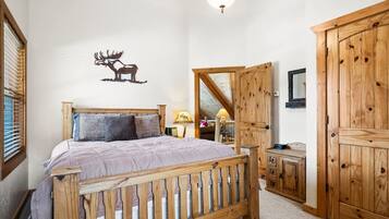 Een slaapkamer met een houten bed, een spiegel, een kledingkast en een herten decoratie aan de muur.