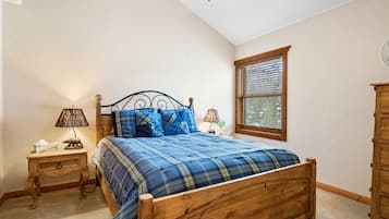 A bedroom with a wooden bed, a nightstand with a lamp, a window with blinds, and a wooden wardrobe.