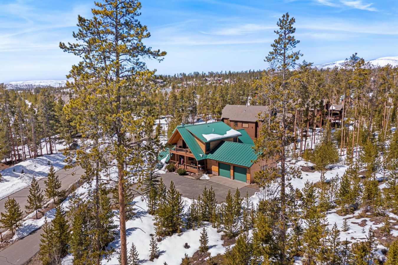 A lodge with a green roof, surrounded by snow-covered ground and trees.