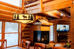 L’intérieur chaleureux d’un chalet avec une cheminée, des murs en bois, un téléviseur et une enseigne suspendue représentant un élan et des arbres.