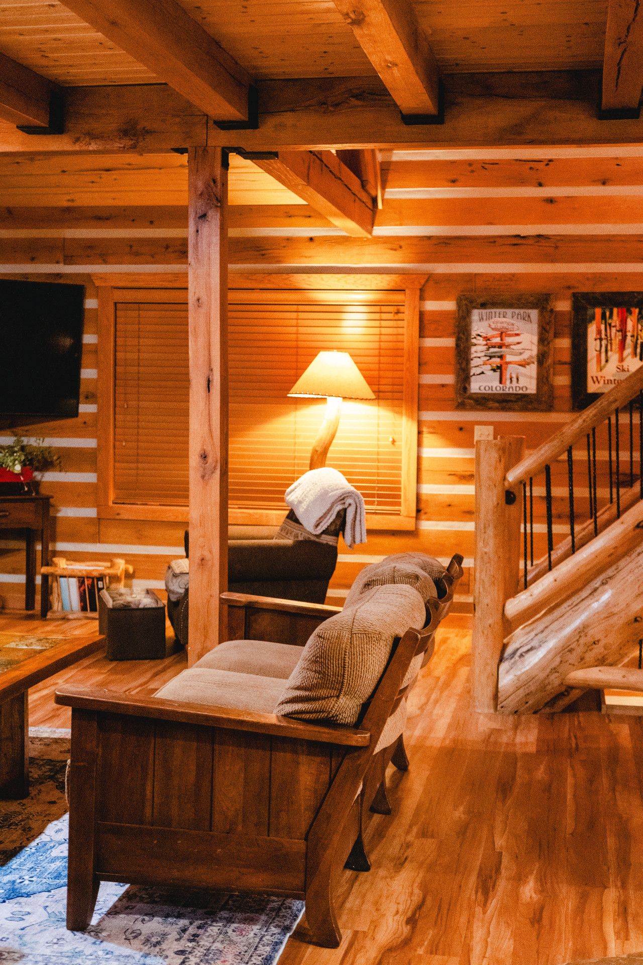 Ein gemütliches Cabin-Interieur mit einer Holztreppe, einer einladenden Lounge mit Sofa und Kissen sowie einer warmen Lampe, die für eine angenehme Beleuchtung sorgt.