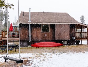 A wooden building with a red trampoline in the yard.
