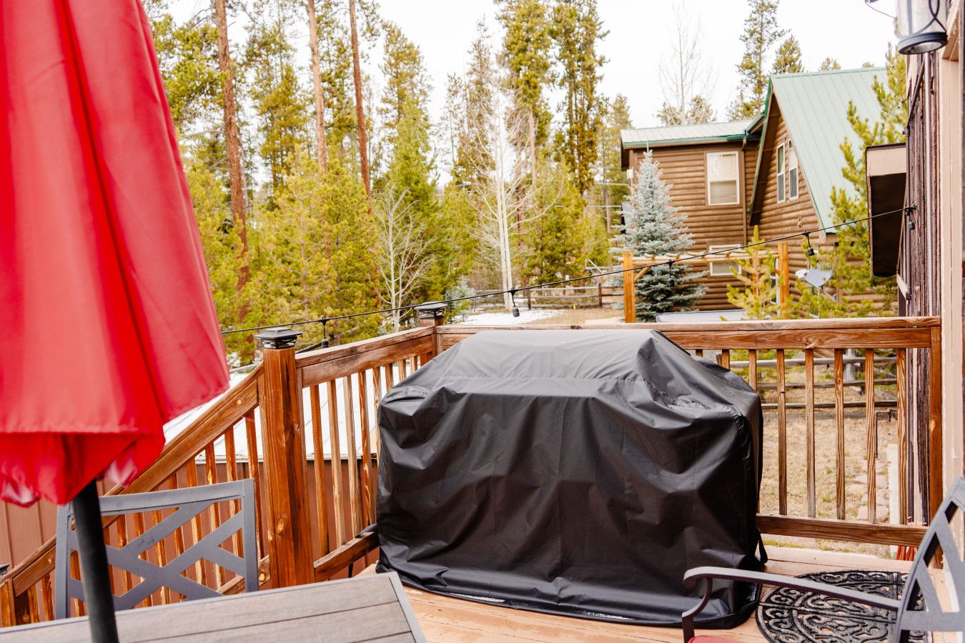 A covered outdoor grill on a wooden deck with a red umbrella and a metal railing.