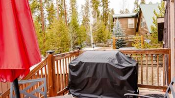 A covered outdoor grill on a wooden deck with a red umbrella and a metal railing.