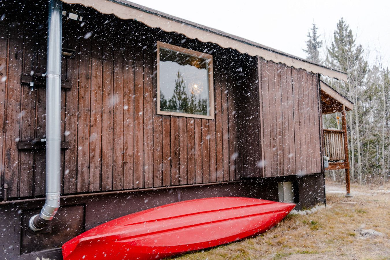 A wooden cabin with a window, a red boat, and a snowy landscape.