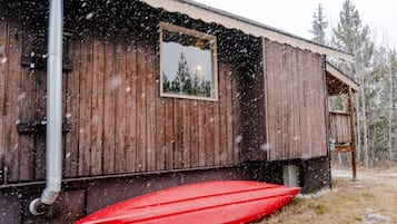 A wooden cabin with a window, a red boat, and a snowy landscape.
