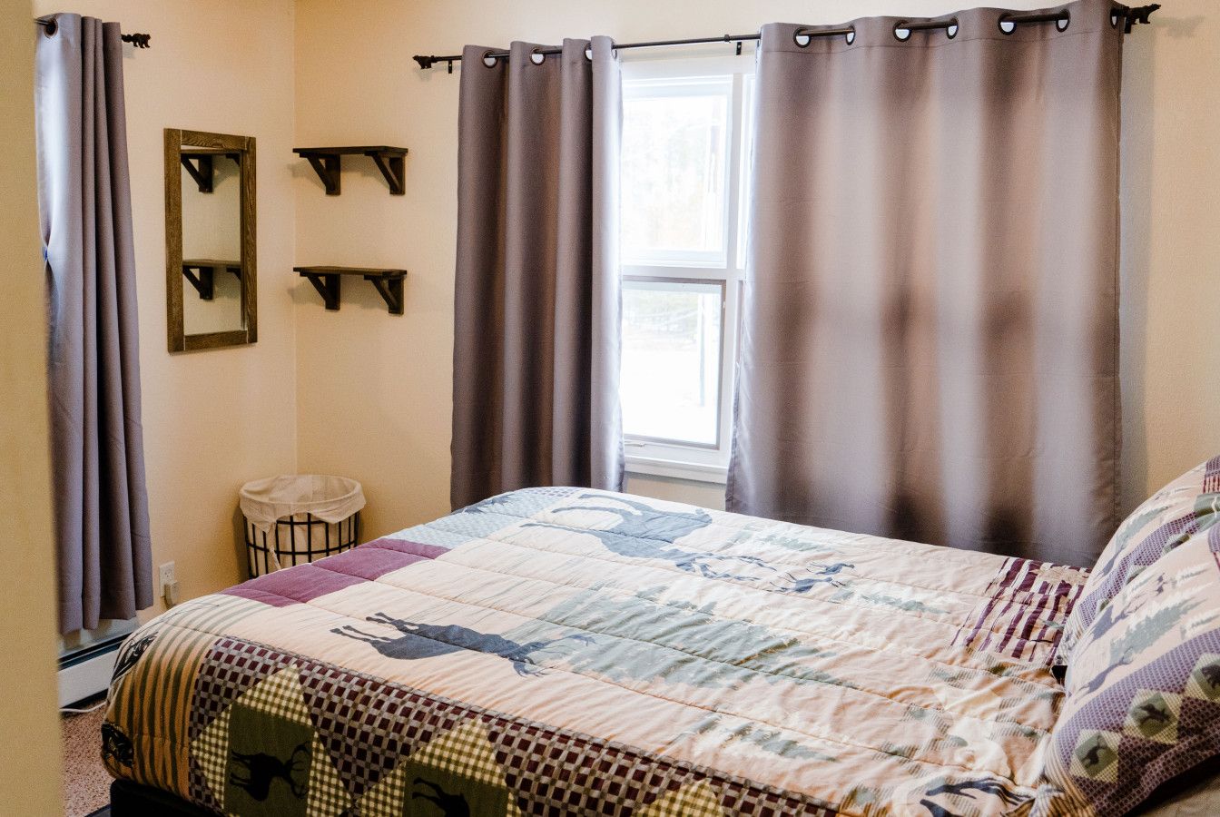 A bedroom with a bed, curtains, a window, and a mirror.