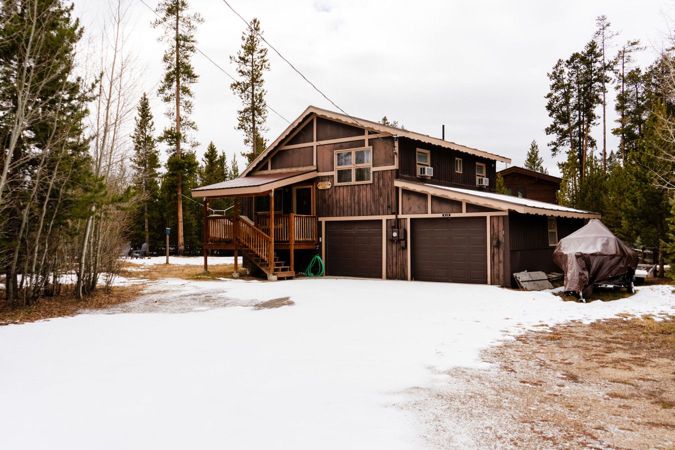 A two-story wooden cabin with a porch, a garage, and a covered outdoor area.