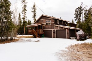 Een houten chalet met twee verdiepingen, een veranda, een garage en een overdekt buitengebied.