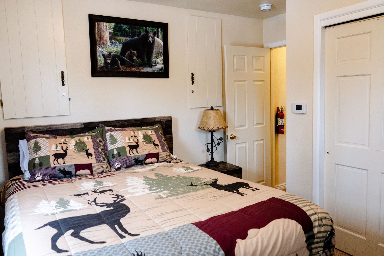 A bedroom with a bed featuring a quilt with animal prints, a wooden headboard, a bedside lamp, and a framed picture on the wall.