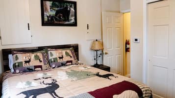 A bedroom with a bed featuring a quilt with animal prints, a wooden headboard, a bedside lamp, and a framed picture on the wall.