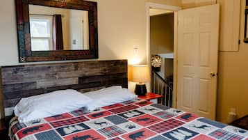 Un dormitorio con cabecera de madera, colcha con estampados de animales, espejo, lámpara y puerta que da a otra habitación.