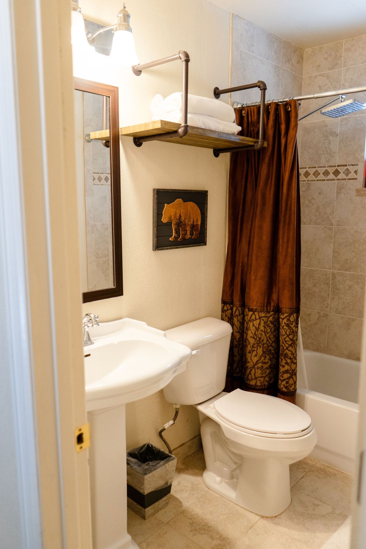 Un baño con lavamanos, inodoro y ducha. Hay un perchero sobre el lavamanos y una cortina de ducha.