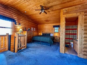 Un dormitorio tipo cabaña de madera con una cama, paredes de madera, un ventilador de techo y vistas al exterior.