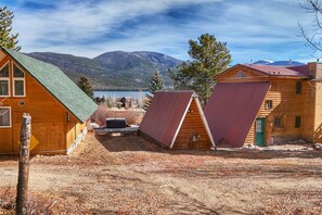 A cabin with a green roof, a red-roofed structure, and a wooden building with a green door, all set against a mountainous backdrop.