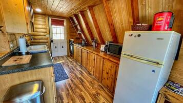 A cabin-style kitchen with wooden walls, a refrigerator, a sink, and a wooden countertop.