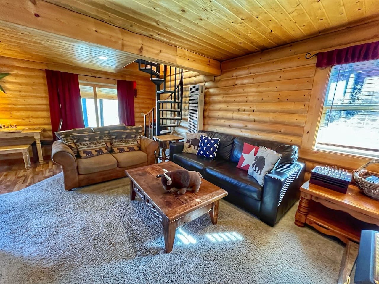 L’intérieur d’un chalet confortable, avec des murs en bois, un escalier en bois, un ensemble de canapés et une table à manger.