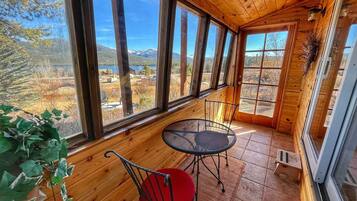 A wooden cabin with large windows offering a view of a mountainous landscape.