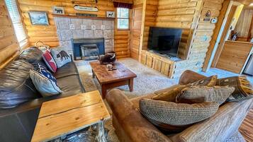 L’intérieur d’un chalet confortable, avec une cheminée, des meubles en bois et un téléviseur.