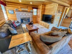 A cozy log cabin interior with a fireplace, wooden furniture, and a television. - Relax in the night sky w/ hot tub (Grand Lake)