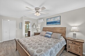Ein Schlafzimmer mit einem Bett, einem Deckenventilator, einem Nachttisch mit Lampe, einem Gemälde und einer Tür.