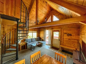A wooden cabin interior with a staircase, a sofa, a coffee table, and a dining table.