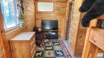 Een gezellig chalet met houten wanden, een televisie, een grote teddybeer en een vloerkleed met dierenprint.