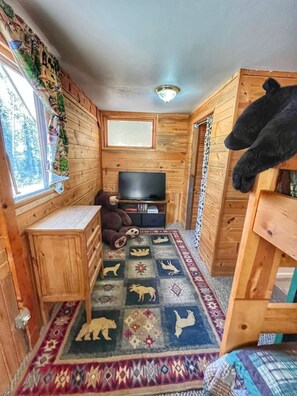 A cozy cabin with wooden walls, a television, a large teddy bear, and a rug with animal prints.