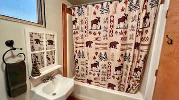 A bathroom with a white sink, a mirror, and a shower curtain with a nature pattern.