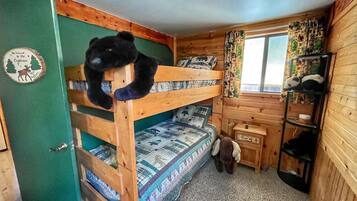 Een slaapkamer met een stapelbed, een houten hoofdbord, een klein houten kastje en een raam met gordijnen.