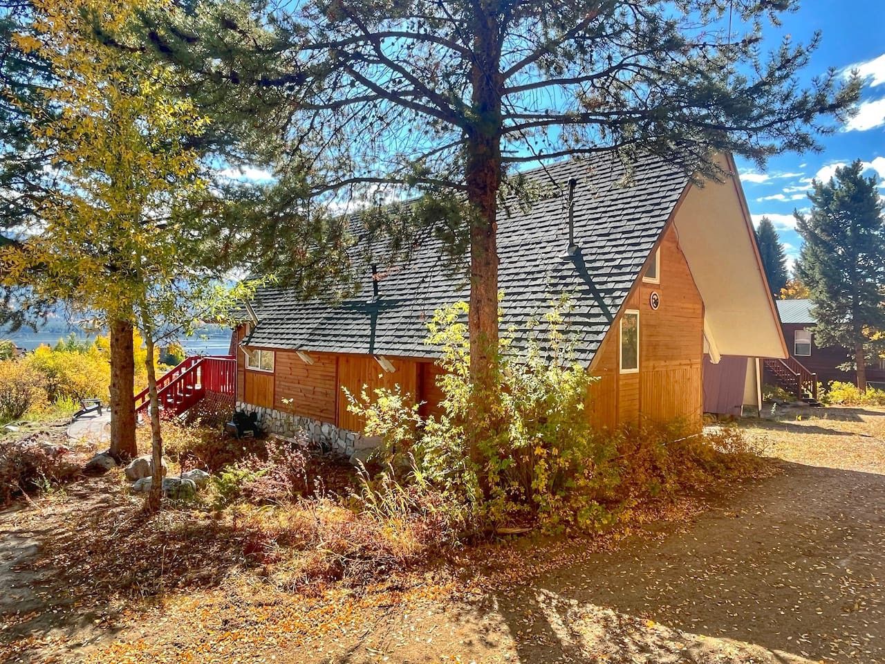 A wooden cabin with a sloped roof, a red staircase, and a view of a lake.