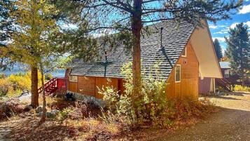 A wooden cabin with a sloped roof, a red staircase, and a view of a lake.