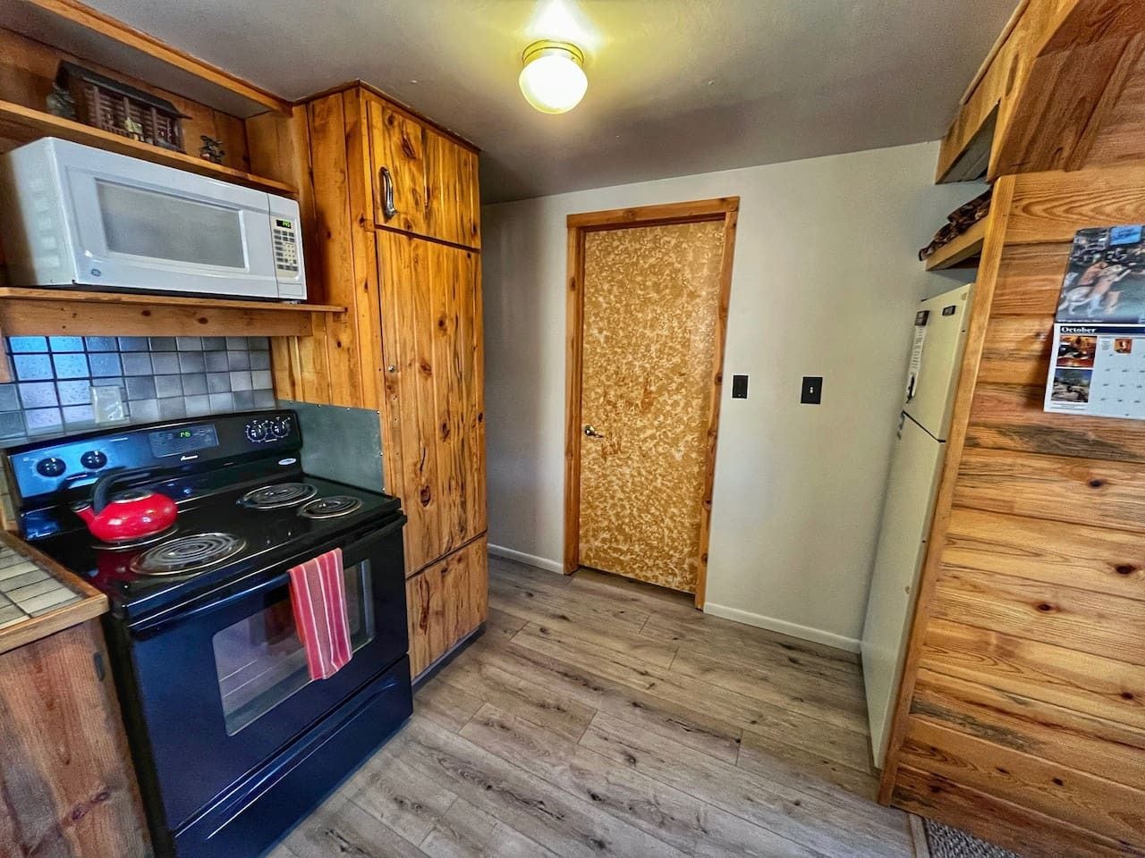 A compact kitchen with wooden cabinets, a black stove, a microwave, and a refrigerator.
