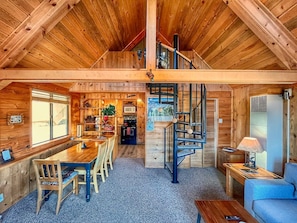 Interior de una cabaña de madera con comedor, cocina y una escalera en espiral.