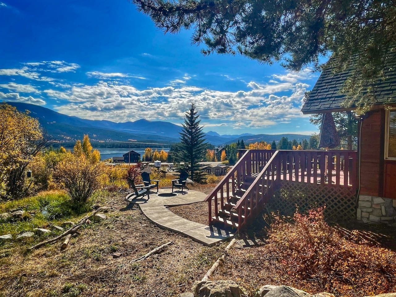 A patio area with outdoor seating, a wooden staircase, and a view of mountains and a lake.