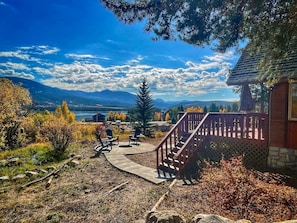 A patio area with outdoor seating, a wooden staircase, and a view of mountains and a lake.
