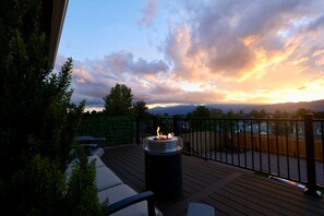 Eine Terrasse mit Feuerstelle, umgeben von Holzzaun und Bäumen, mit Blick auf ein Wohngebiet.