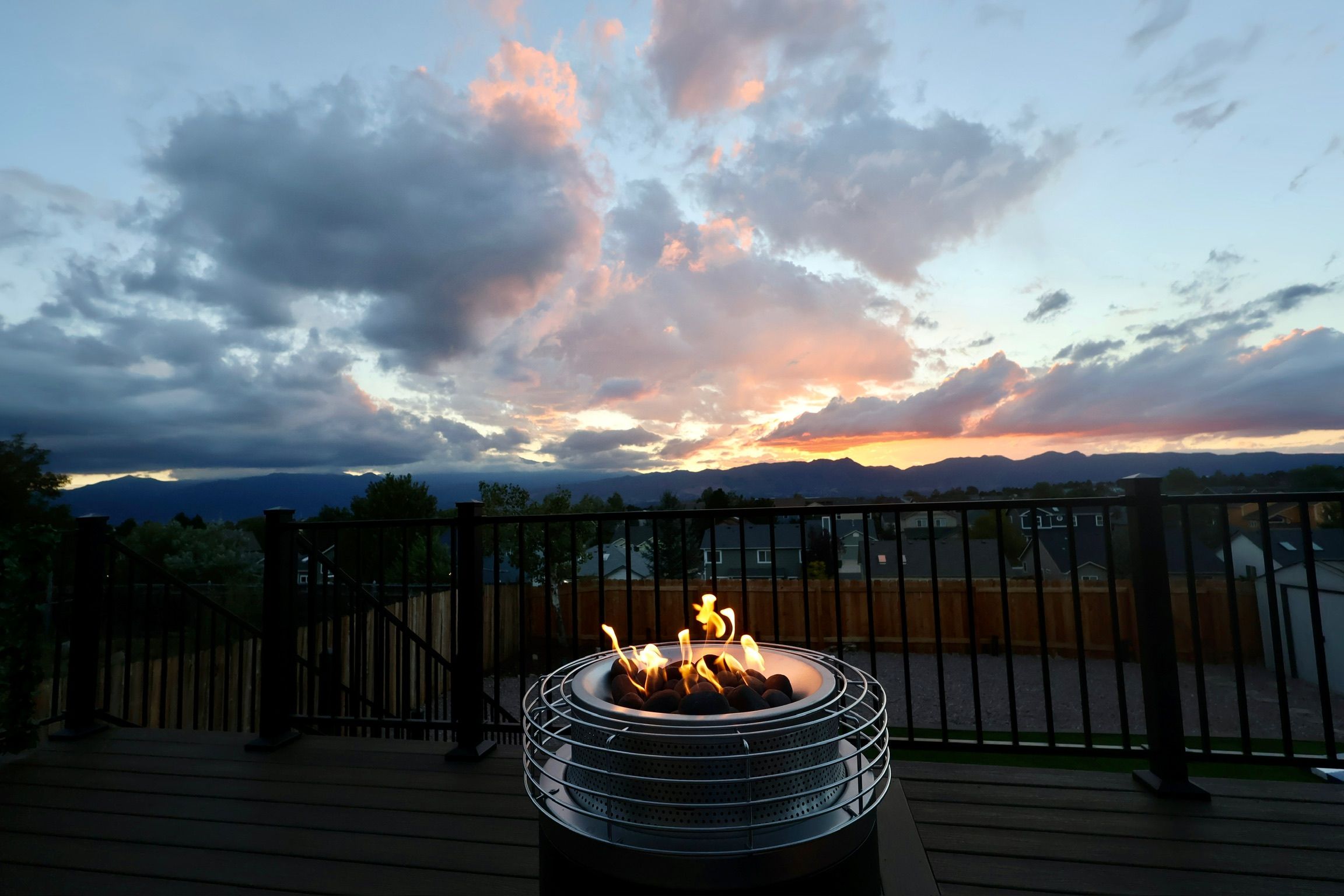A deck with a metal fire pit in the center, surrounded by a wooden deck and a metal railing.