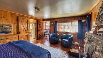 Une pièce rustique comprenant un lit, deux fauteuils en cuir, un mur en pierre et un lambris en bois.