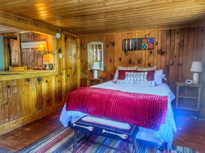 A wooden-paneled bedroom with a bed, a nightstand, a lamp, and a wall clock. - 1 BR with sunroom-walk to beach (Grand Lake)