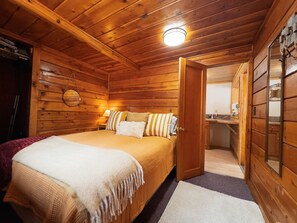 A wooden cabin bedroom with a bed, pillows, and a nightstand. There is a door leading to a bathroom and a kitchenette. - 1 BR w/ futon-short walk to lake (Grand Lake)