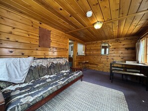Ein Ferienhausinnenraum mit Holzbalkendecke, einer Couch mit gemustertem Überwurf, einem Esstisch und einem kleinen Fenster.